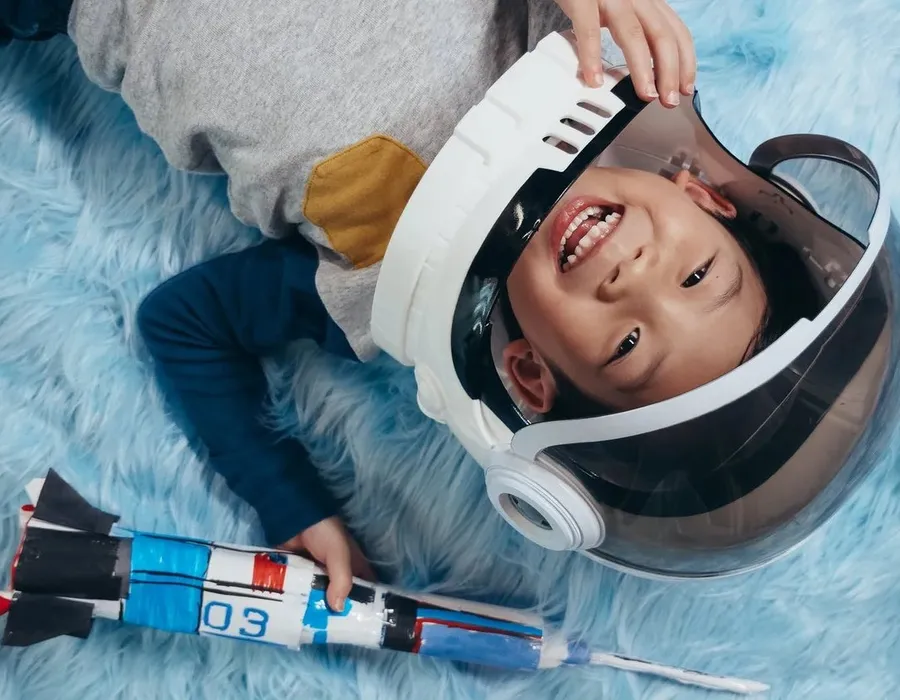 A child in an astronaut costume, lying on the floor and looking up