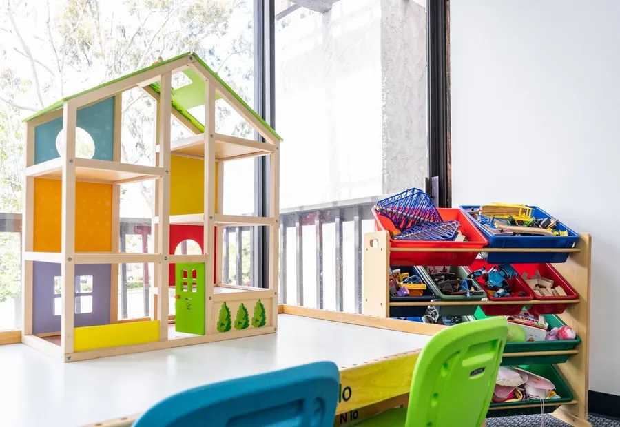 Wooden dollhouse and toy bins by a sunny window in the play-therapy room